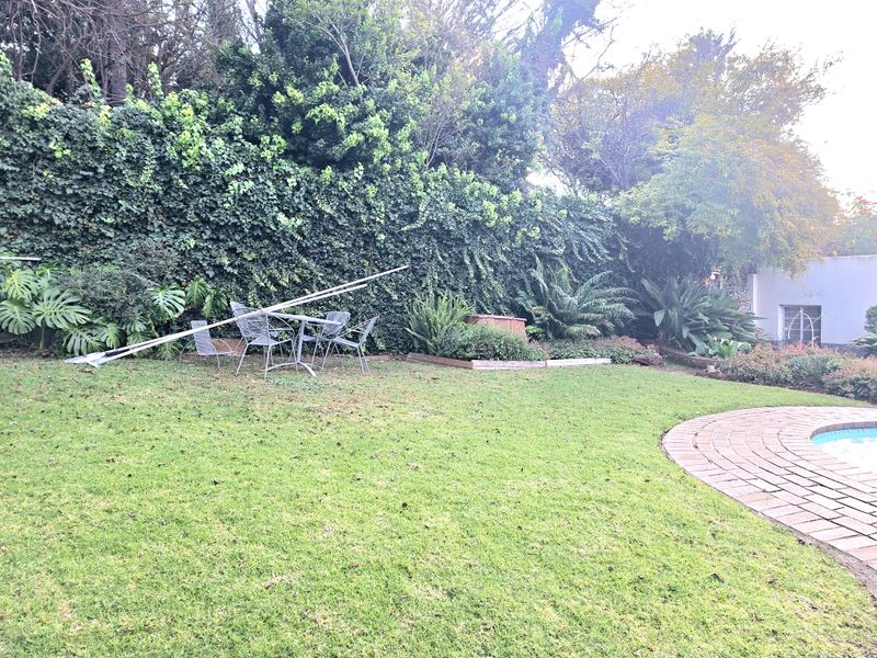 A private garden area featuring a well-maintained lawn, established greenery, and a swimming pool with brick surround.