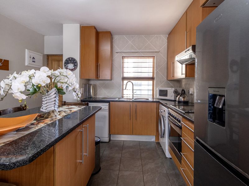 A functional kitchen featuring wood-finish cabinetry, granite countertops, a tiled backsplash, and integrated appliances including an oven and hob.
