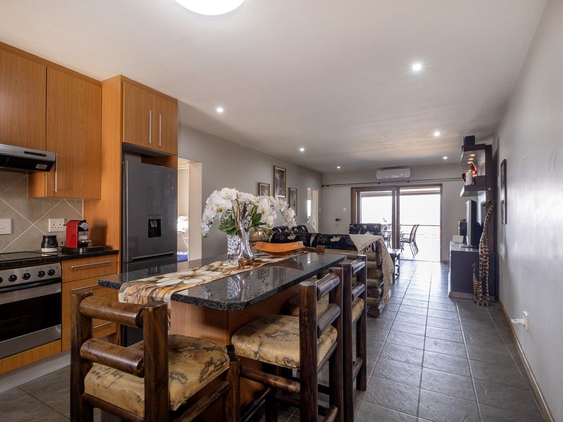 Open-plan living area featuring a modern kitchen with granite countertops, built-in appliances, and tiled flooring, leading to a bright lounge with balcony access.