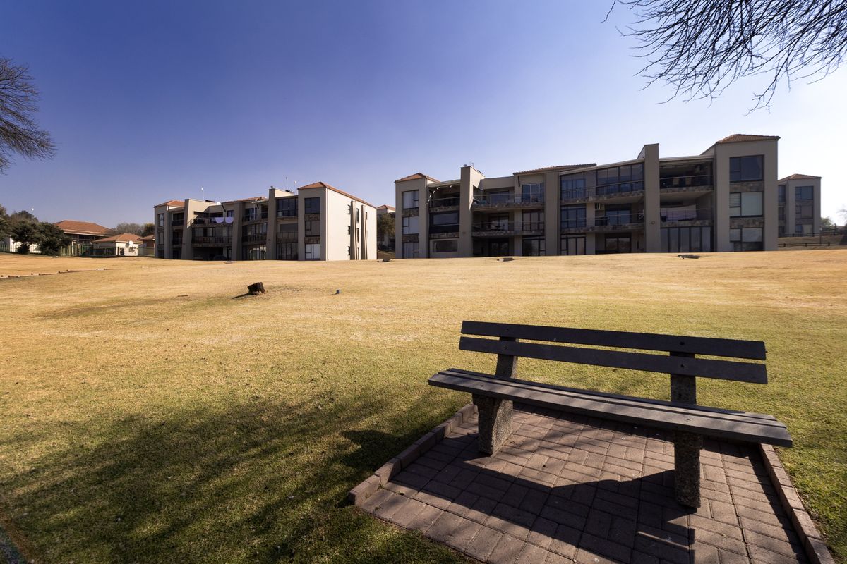 A wide-angle view of the rear exterior of a multi-story apartment complex featuring communal lawn areas and private balconies.