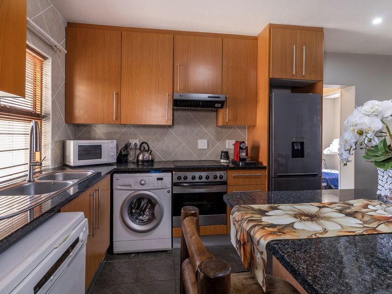 A functional kitchen featuring wood-finish cabinetry, granite countertops, a double sink, and integrated appliances including an oven, hob, and extractor fan.