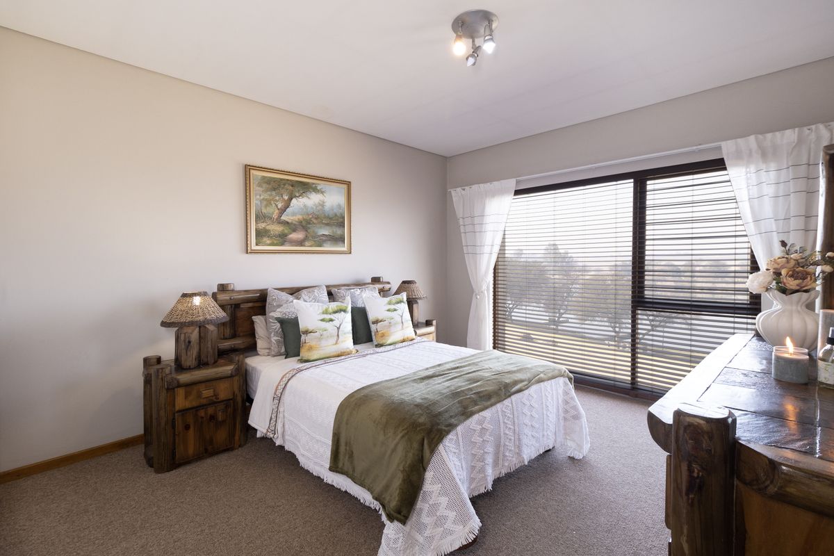 A well-maintained bedroom featuring neutral walls, carpeted flooring, and a large sliding glass door with venetian blinds providing natural light.