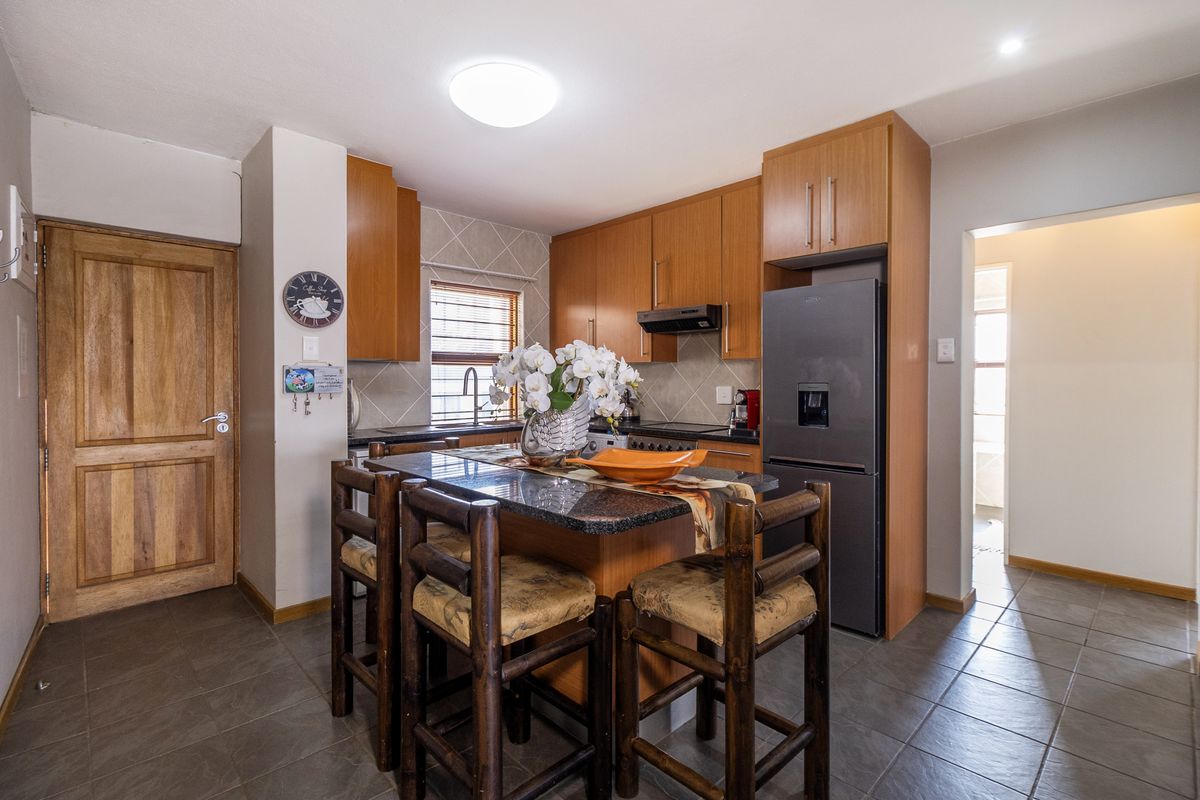 Functional kitchen featuring wooden cabinetry, granite countertops, tiled backsplash, and integrated appliances, offering a practical layout with a central breakfast bar area.
