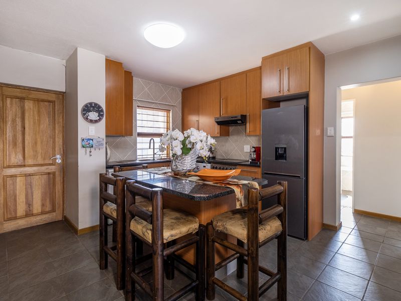 Functional kitchen featuring wooden cabinetry, granite countertops, tiled backsplash, and integrated appliances, offering a practical layout with a central breakfast bar area.