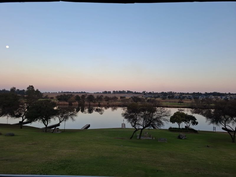 A scenic view overlooking a tranquil lake, landscaped green lawns, and distant residential properties at dusk.