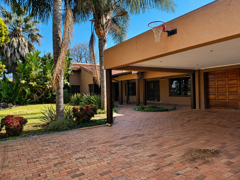 Front exterior view featuring a brick driveway, covered patio area, wooden garage door, and established garden landscaping.
