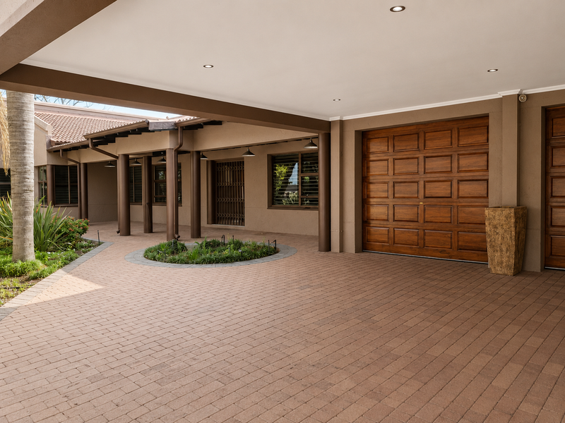 A well-maintained front exterior featuring a spacious paved driveway, covered entrance area, recessed lighting, and a high-quality wooden garage door.