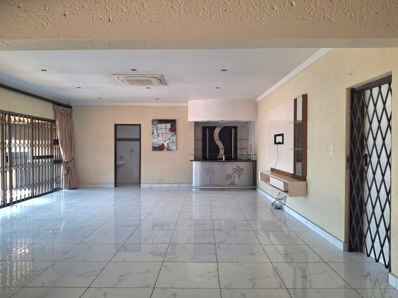 Spacious living area featuring tiled flooring, a built-in bar, ceiling-mounted air conditioning, and security gates, offering a versatile open-plan layout.