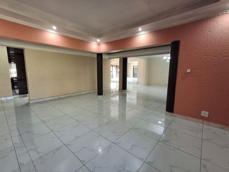 Spacious open-plan living area featuring large-format porcelain floor tiles, structural columns, and recessed ceiling lighting with decorative cornicing.