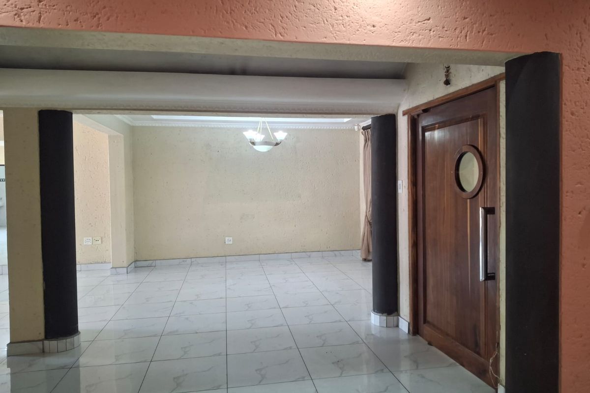 An empty living area featuring tiled flooring, structural columns, and a distinctive wooden door with a porthole window.