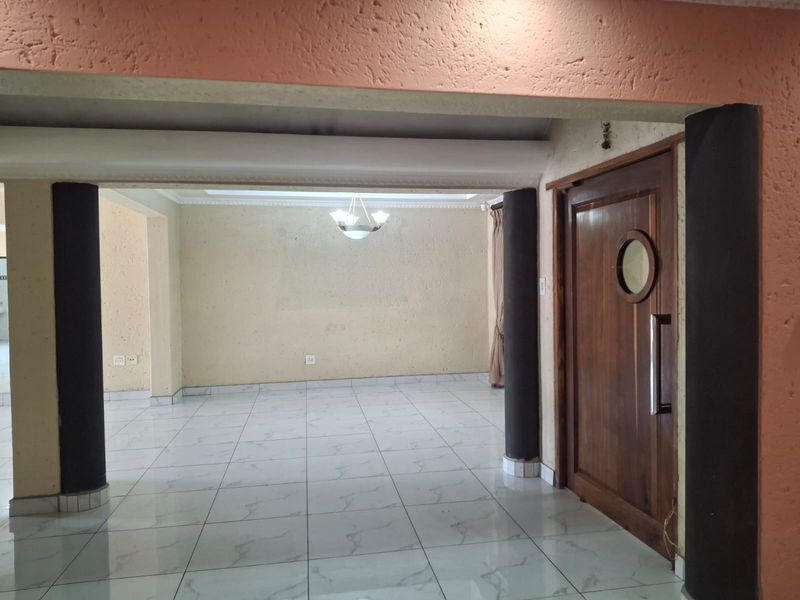 An empty living area featuring tiled flooring, structural columns, and a distinctive wooden door with a porthole window.