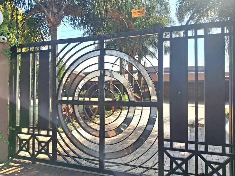 A secure front entrance featuring a decorative metal gate, electric fencing, and a paved driveway leading to the property.