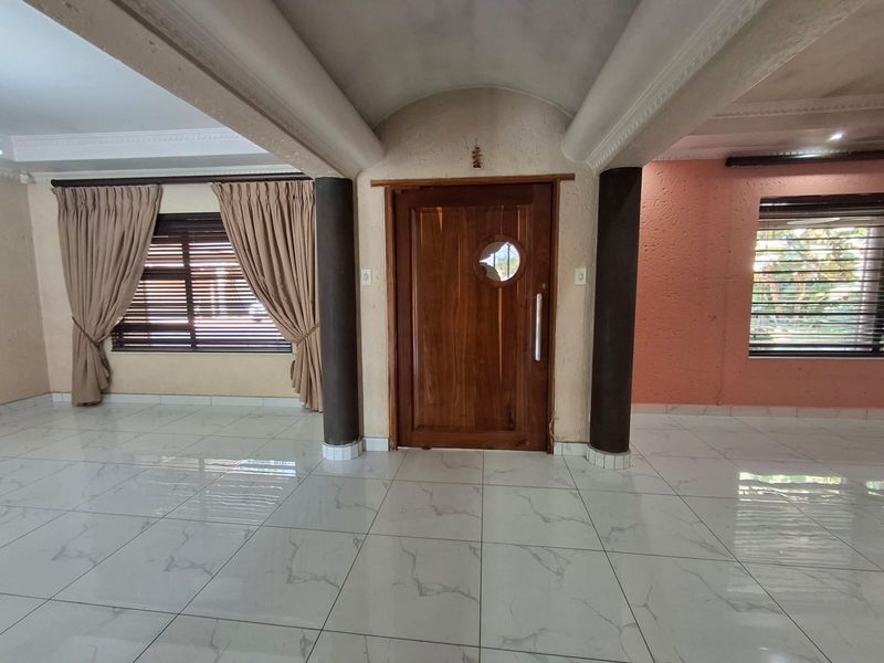 Spacious entrance hall featuring a unique timber porthole door, vaulted ceilings, structural columns, and modern marble-look tiled flooring.