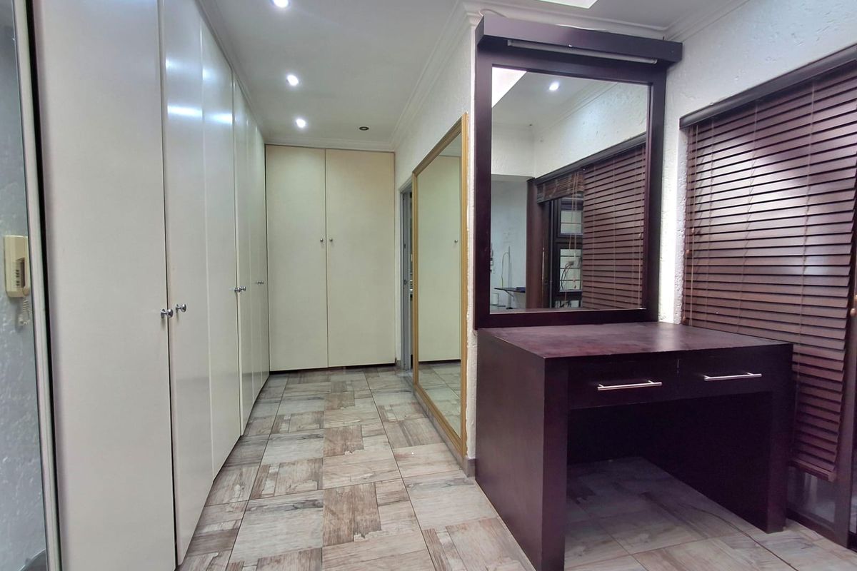 A spacious dressing area featuring extensive built-in cupboards, a dedicated vanity station with an integrated mirror, and modern tiled flooring.