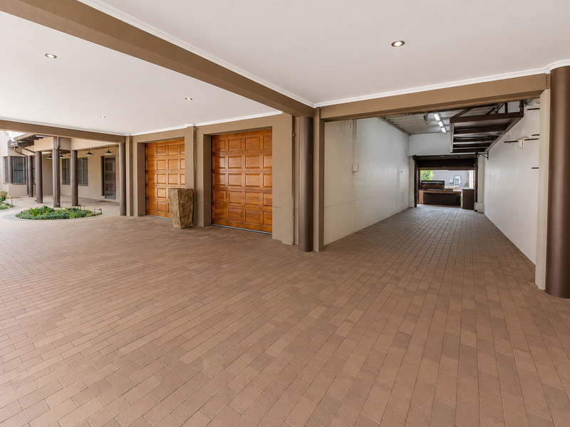 Spacious covered parking area featuring paved flooring, recessed lighting, and multiple wooden garage doors, providing ample space for vehicles.