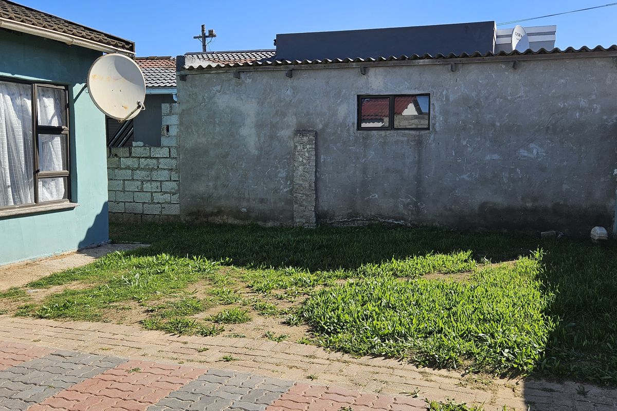 A rear exterior view of the property featuring a paved area, a small lawn, and boundary walls with weathered finishes.