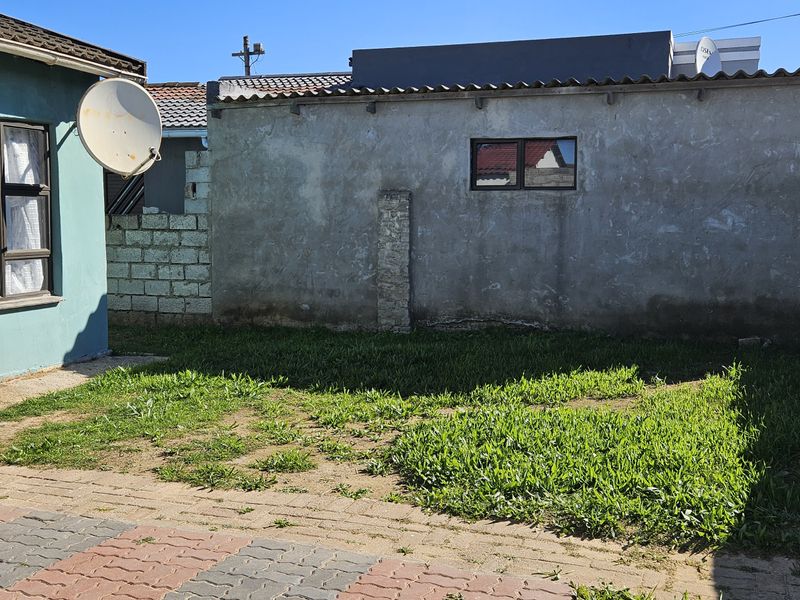 A rear exterior view of the property featuring a paved area, a small lawn, and boundary walls with weathered finishes.