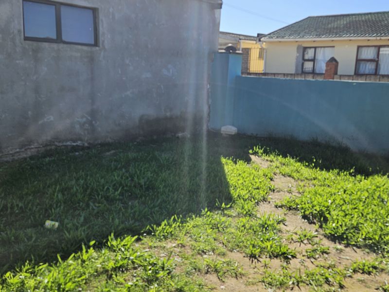 A rear exterior view of the property featuring a small garden area enclosed by a boundary wall and plastered exterior building facade.