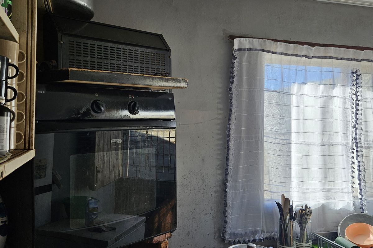 A kitchen area featuring a built-in oven and extractor fan, with visible wear on the wall surfaces requiring maintenance or renovation.