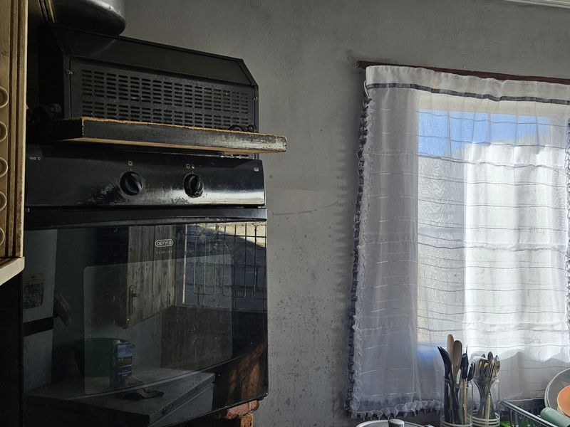 A kitchen area featuring a built-in oven and extractor fan, with visible wear on the wall surfaces requiring maintenance or renovation.