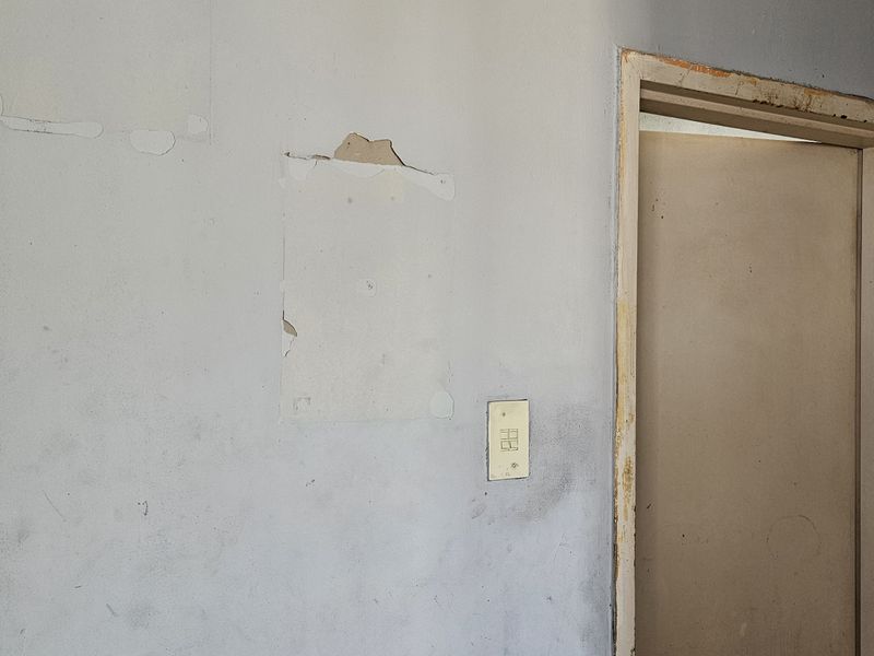 A hallway interior showing significant wear to the wall surfaces and door frames, requiring cosmetic repair and repainting.