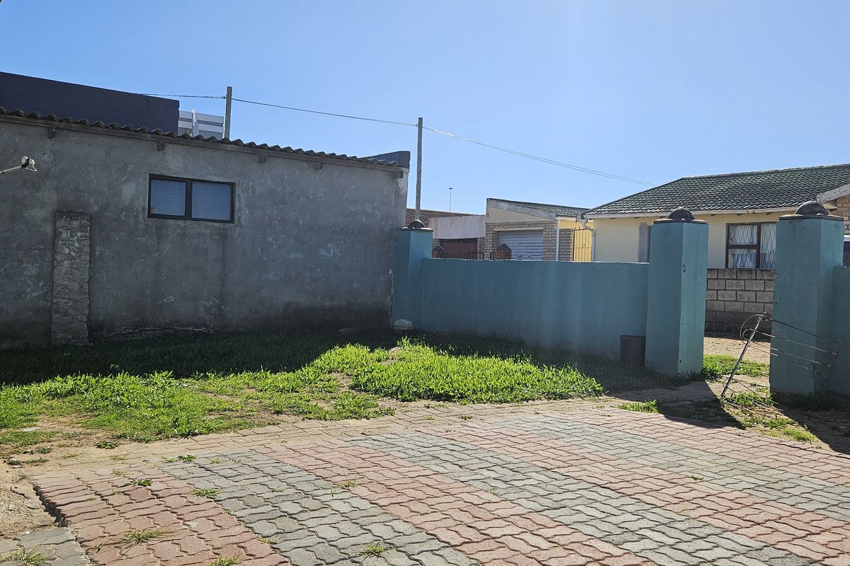 A rear exterior view of the property featuring a paved driveway area and a boundary wall with a satellite dish mounted on the side.
