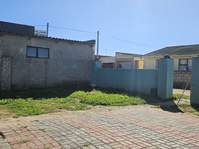 A rear exterior view of the property featuring a paved driveway area and a boundary wall with a satellite dish mounted on the side.