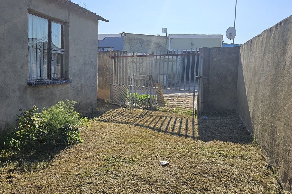 A rear exterior view of the townhouse featuring a small lawn area, perimeter boundary walls, and a metal security gate.