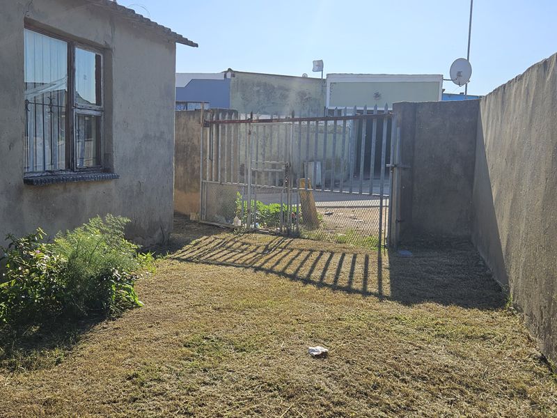 A rear exterior view of the townhouse featuring a small lawn area, perimeter boundary walls, and a metal security gate.