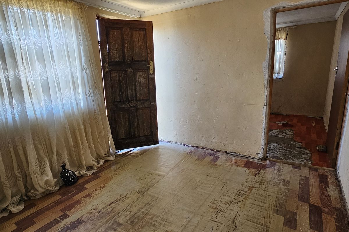 An empty living room area featuring worn laminate flooring and visible wall damage, requiring renovation to restore its functional appeal.