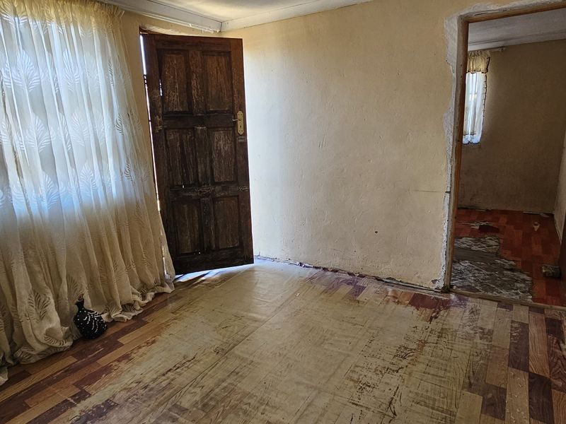 An empty living room area featuring worn laminate flooring and visible wall damage, requiring renovation to restore its functional appeal.
