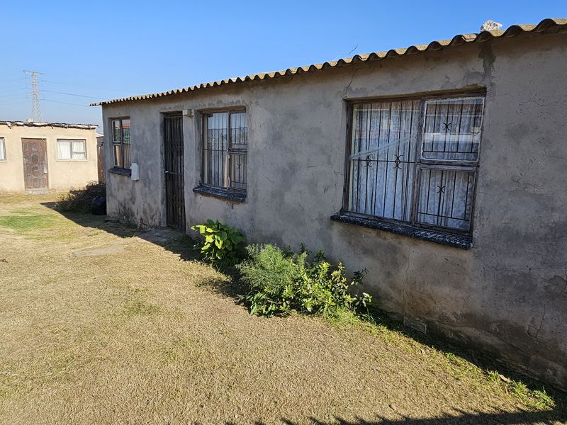 Rear exterior view of a townhouse featuring a basic plaster finish, metal security bars on windows, and a small yard area.