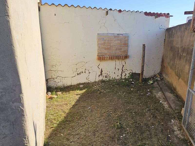 A small, enclosed rear outdoor area featuring a boundary wall with visible plaster cracking and a metal security gate.
