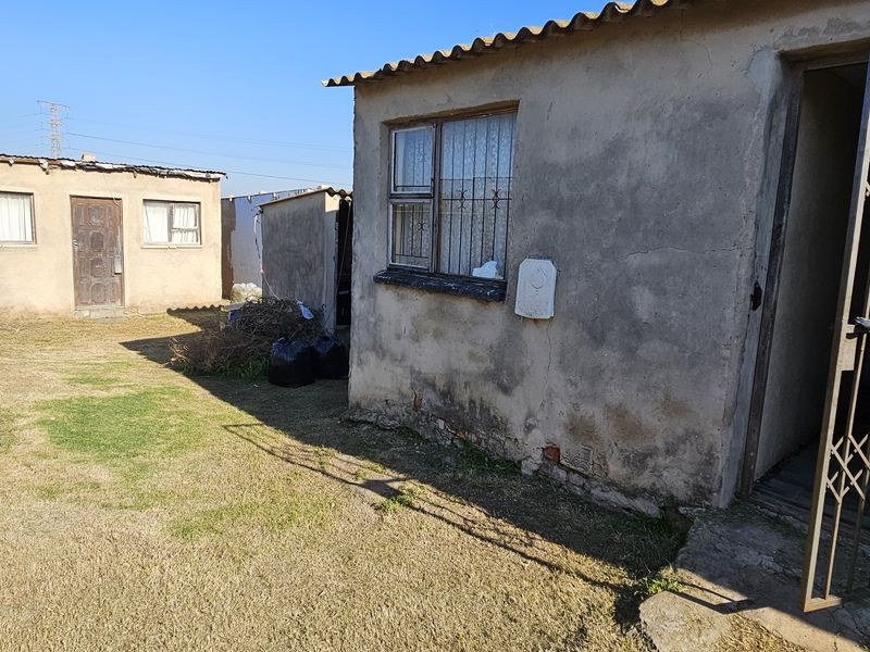 Rear exterior view of a townhouse property featuring concrete masonry walls, security gates, and burglar bars on windows, set within a basic yard area.