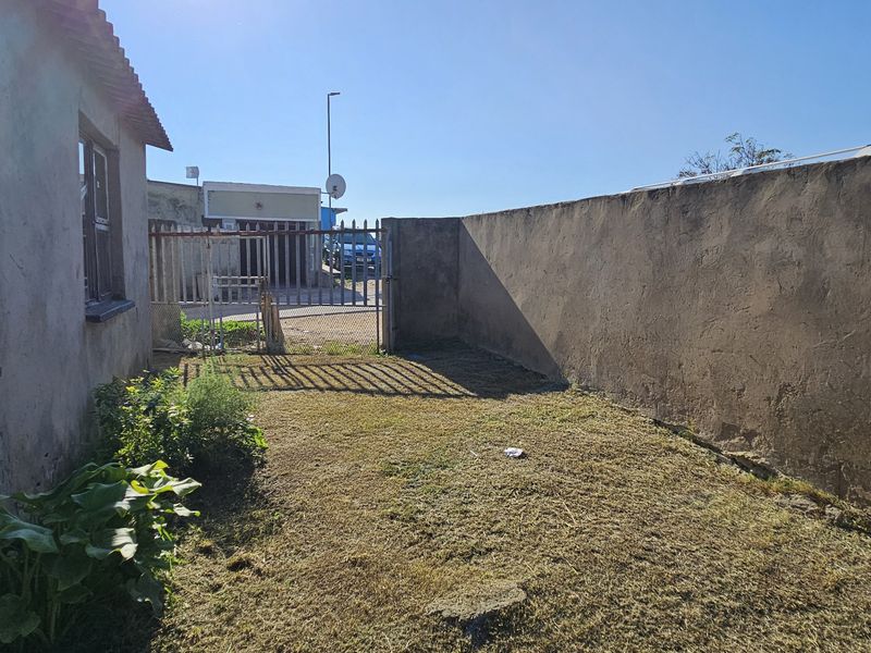 A rear exterior view of the townhouse featuring a small lawn area, perimeter boundary wall, and a metal security gate.