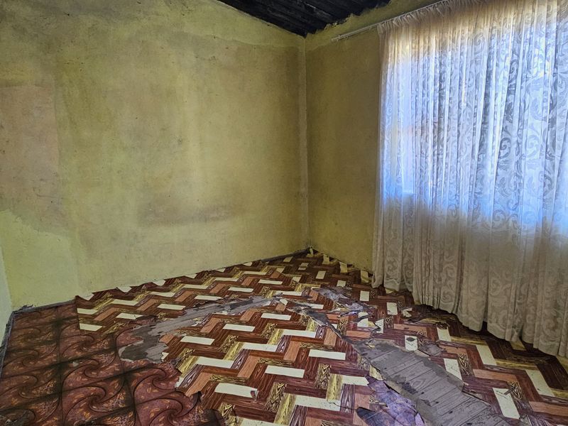 A vacant bedroom requiring significant renovation, featuring damaged flooring and walls in need of repair and repainting.