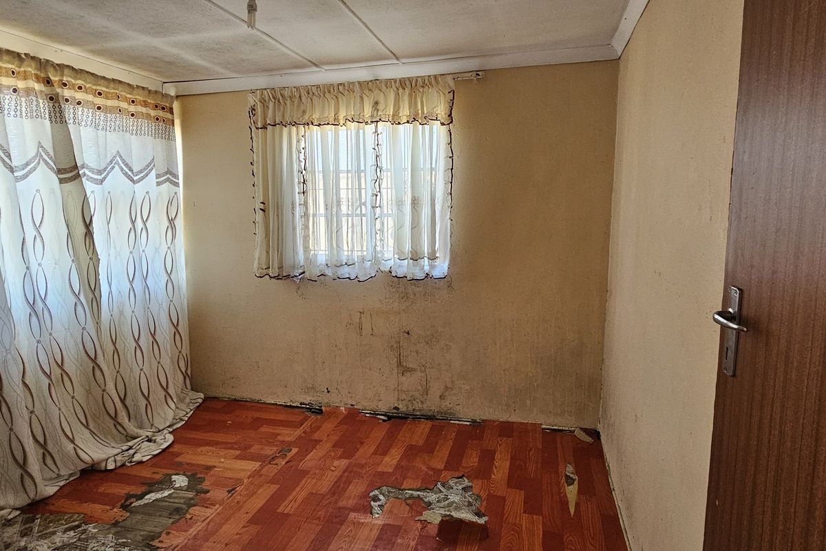 An empty bedroom featuring worn flooring and wall surfaces requiring maintenance and cosmetic updates to restore the space.