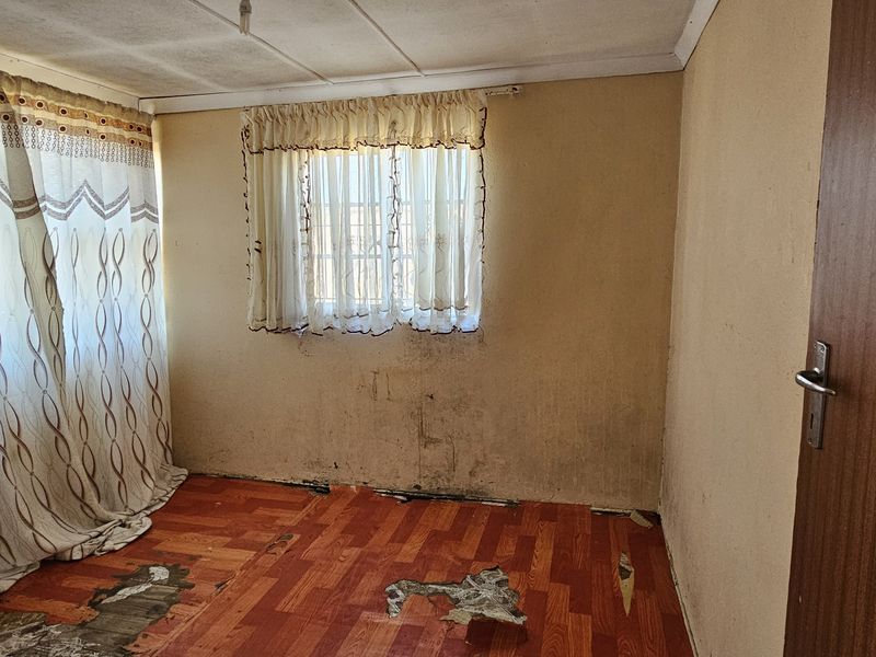 An empty bedroom featuring worn flooring and wall surfaces requiring maintenance and cosmetic updates to restore the space.