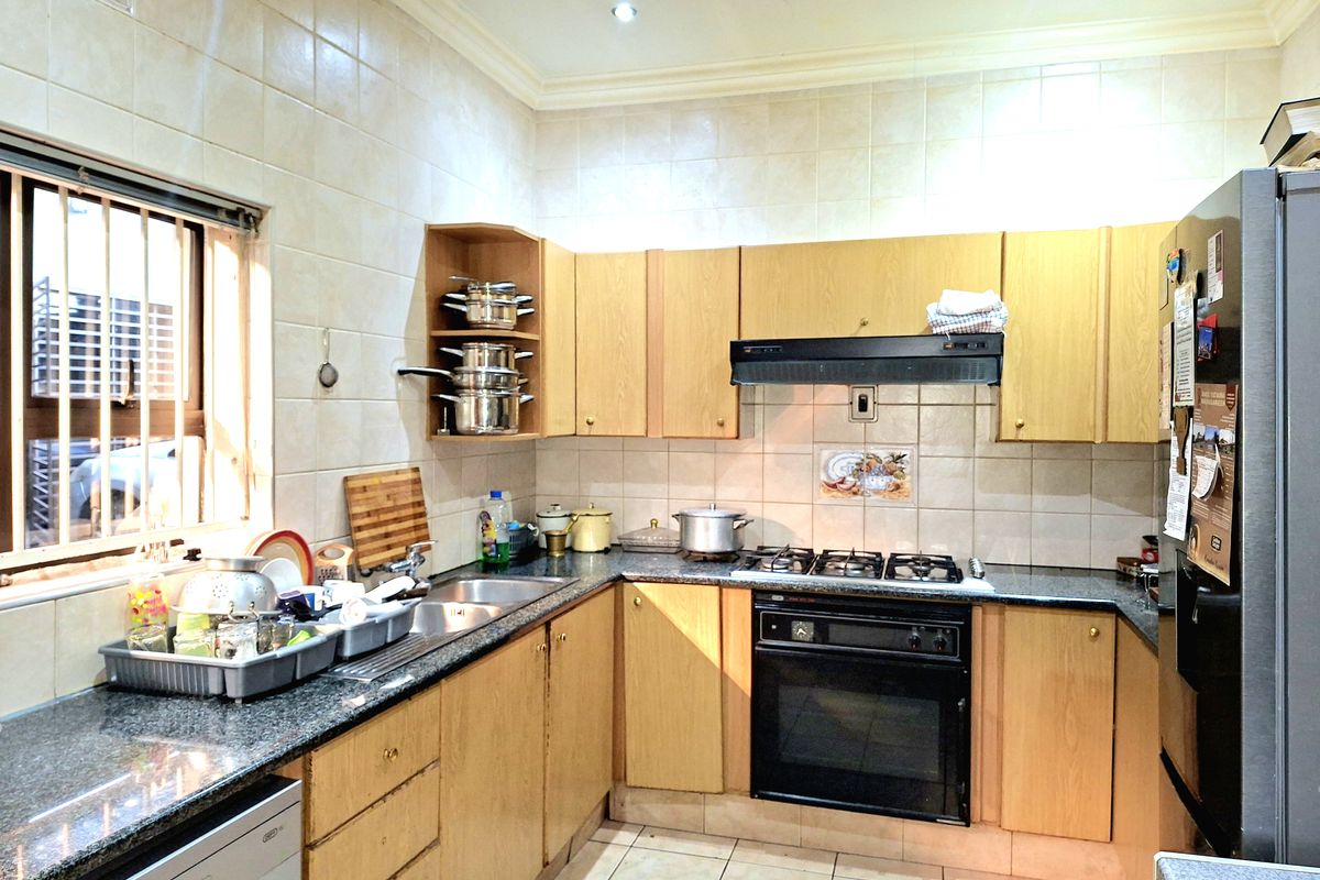 A functional kitchen featuring light wood cabinetry, granite countertops, a built-in oven with gas hob, and tiled finishes throughout.