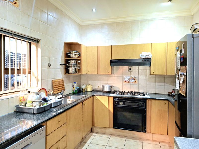 A functional kitchen featuring light wood cabinetry, granite countertops, a built-in oven with gas hob, and tiled finishes throughout.