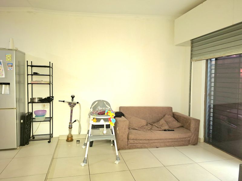 A living area featuring tiled flooring and a roller shutter door, currently requiring cosmetic updates to the walls and ceiling.