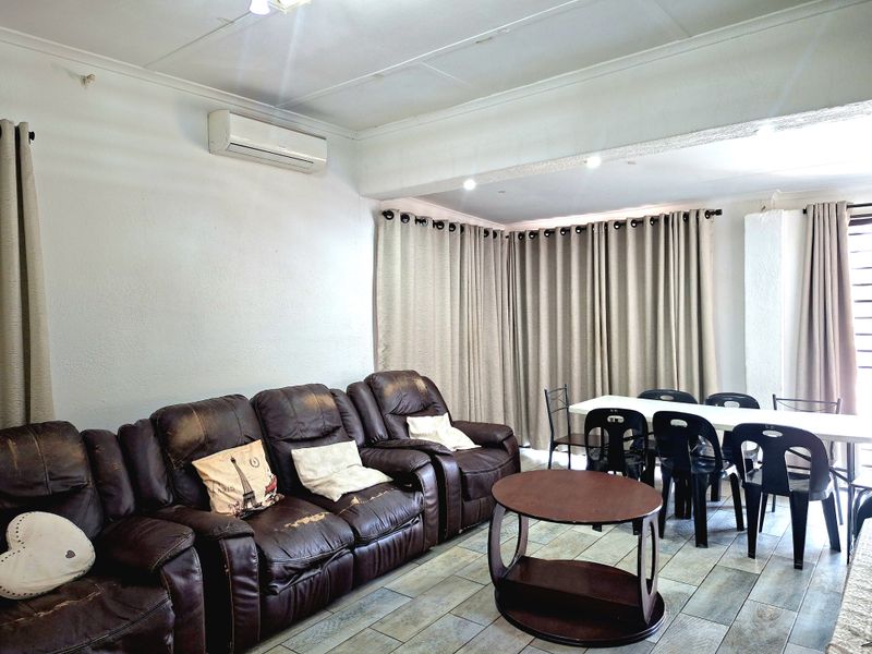 Open-plan living and dining area featuring tiled flooring, recessed ceiling lighting, and a wall-mounted split-system air conditioner.