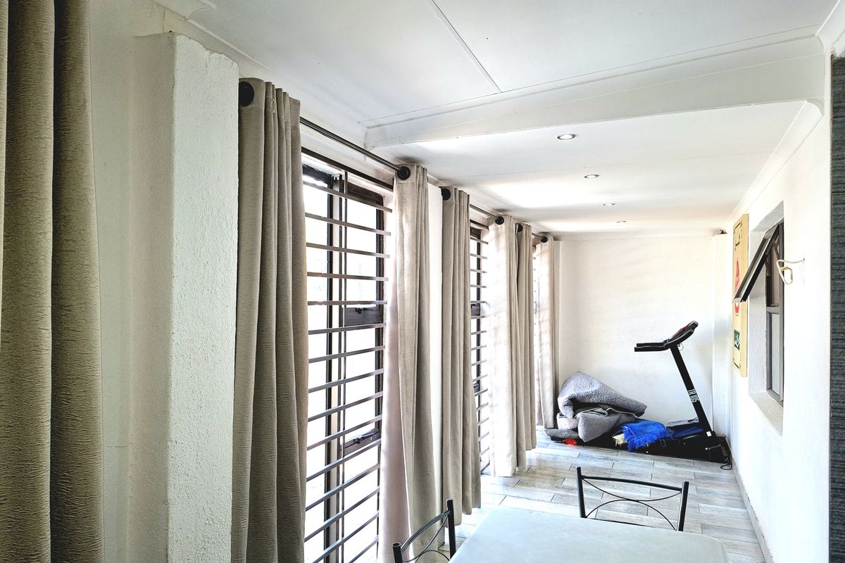A bright living area featuring tiled flooring, recessed downlighting, and large windows fitted with security bars and curtain tracks.