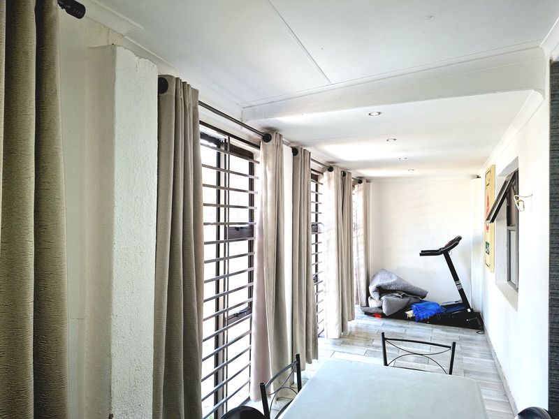 A bright living area featuring tiled flooring, recessed downlighting, and large windows fitted with security bars and curtain tracks.