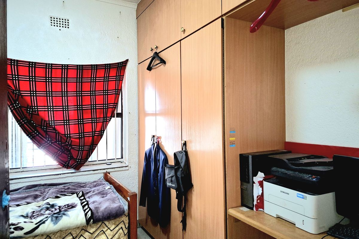 A bedroom featuring built-in wooden cupboards and security bars on the window, requiring cosmetic updates to the wall finishes.