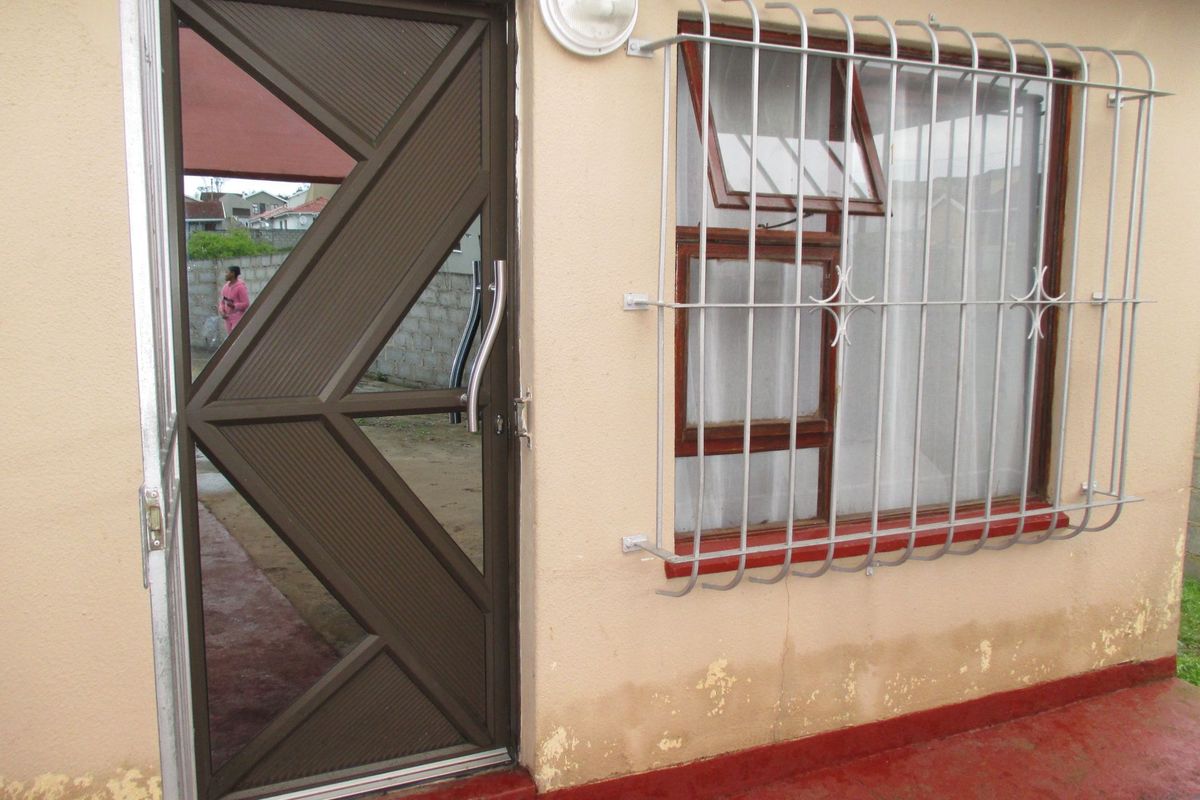Rear exterior view showing a security gate, window with security bars, and exterior wall with visible signs of damp and paint deterioration.