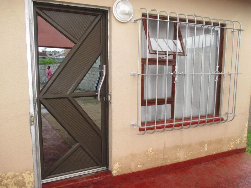 Rear exterior view showing a security gate, window with security bars, and exterior wall with visible signs of damp and paint deterioration.