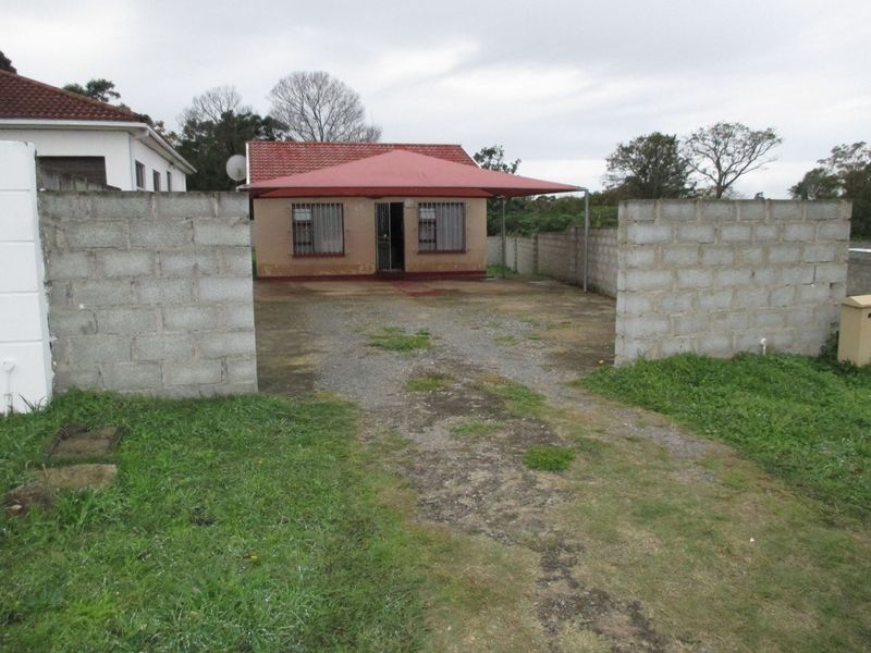 Front view of a detached house featuring a gravel driveway, concrete block boundary walls, and a red tiled roof with a shade cloth carport.