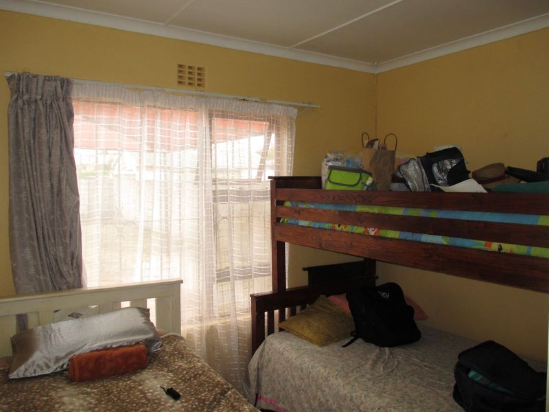 A bedroom featuring a ventilation brick and cove cornice, currently utilized with multiple beds. The space would benefit from a fresh coat of paint.