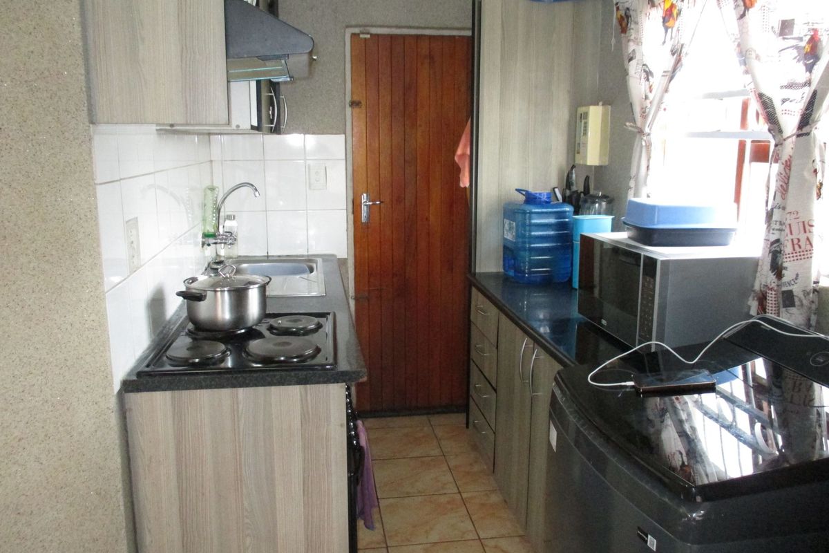 Compact kitchen featuring laminate cabinetry, granite countertops, electric hob, extractor fan, and tiled backsplash with direct access to an exterior timber door.